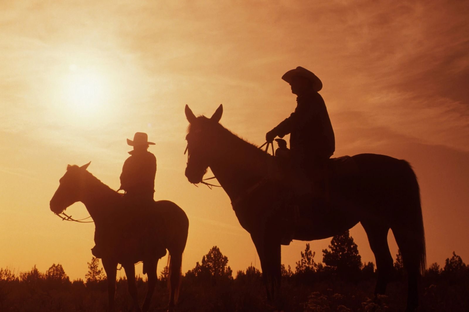 Two riders on horseback silhouetted at sunset
